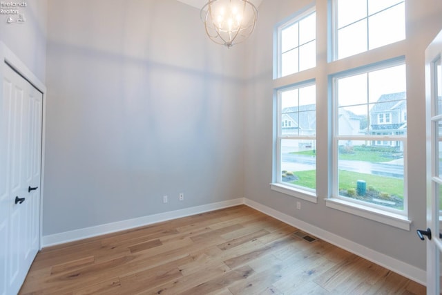 unfurnished room with baseboards, visible vents, a towering ceiling, light wood-type flooring, and a chandelier