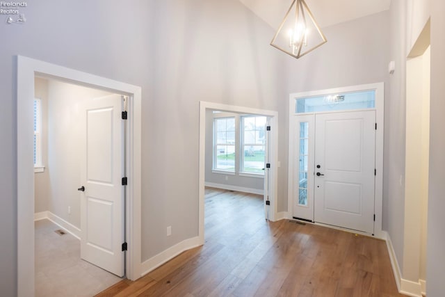 foyer entrance featuring a towering ceiling, light wood-style floors, and baseboards