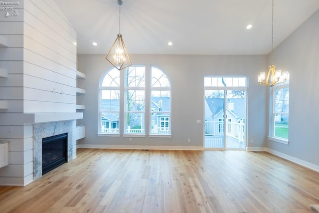 unfurnished living room featuring a chandelier, a tile fireplace, and light wood-style flooring