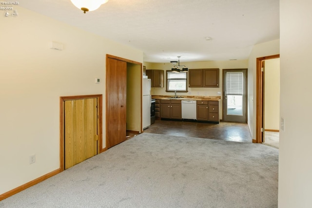 kitchen featuring white appliances, dark carpet, hanging light fixtures, and sink