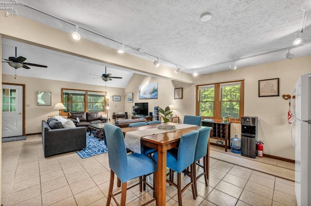 tiled dining space featuring ceiling fan, a textured ceiling, lofted ceiling, and rail lighting