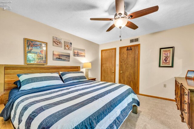 bedroom featuring carpet, ceiling fan, a textured ceiling, and multiple closets