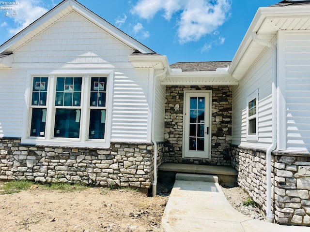 doorway to property featuring stone siding and a shingled roof