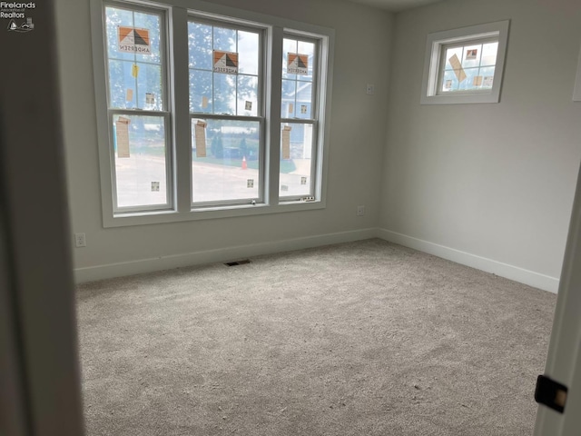 spare room with a healthy amount of sunlight, carpet, visible vents, and baseboards