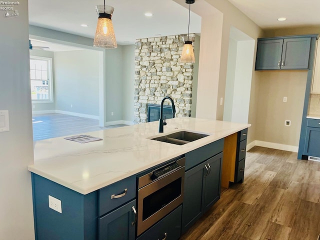 kitchen with dark wood-style floors, light stone counters, a sink, and pendant lighting