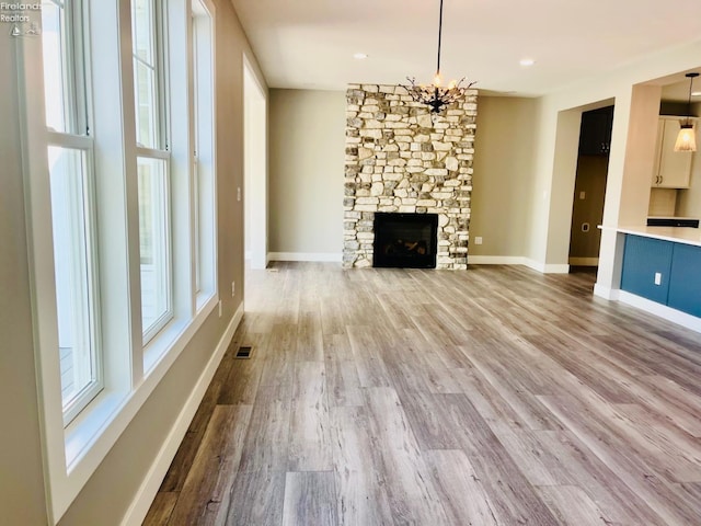 unfurnished living room featuring a fireplace, visible vents, an inviting chandelier, wood finished floors, and baseboards