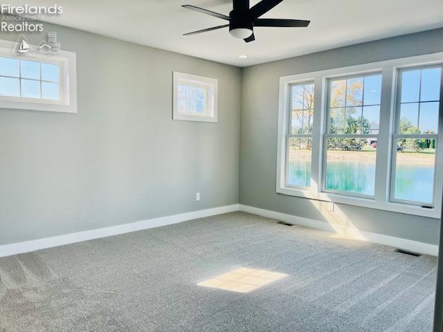 carpeted empty room featuring ceiling fan, visible vents, and baseboards