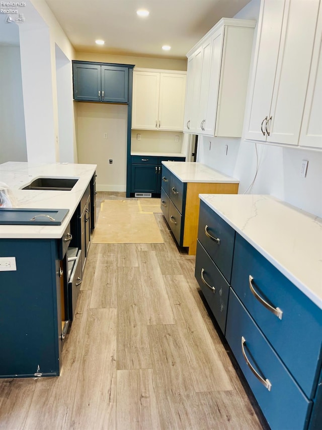 kitchen with white cabinets, a center island, light stone countertops, blue cabinetry, and light wood-style floors