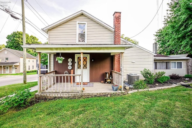 view of front of home featuring a garage, covered porch, cooling unit, and a front yard