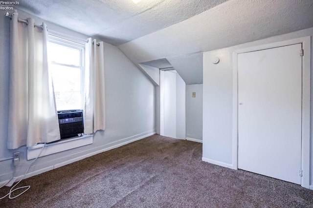 additional living space featuring a textured ceiling, lofted ceiling, and dark carpet