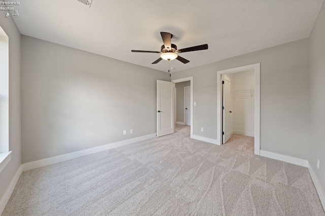 unfurnished bedroom featuring a walk in closet, a closet, light colored carpet, and ceiling fan