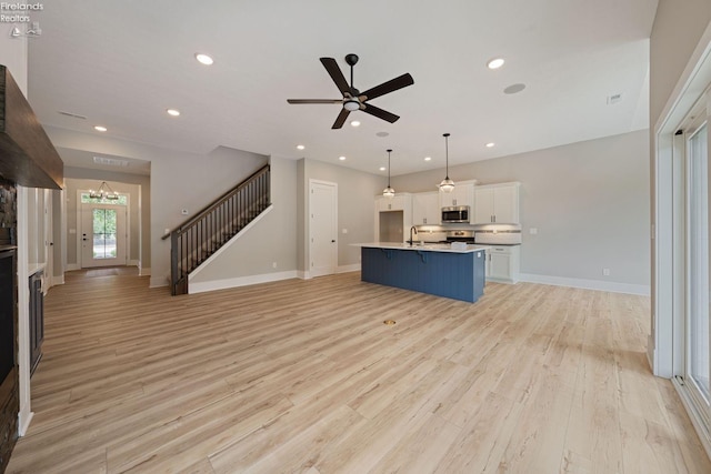 unfurnished living room with sink, light hardwood / wood-style flooring, and ceiling fan with notable chandelier