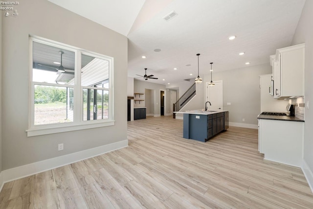 kitchen with sink, an island with sink, blue cabinets, white cabinetry, and light hardwood / wood-style floors