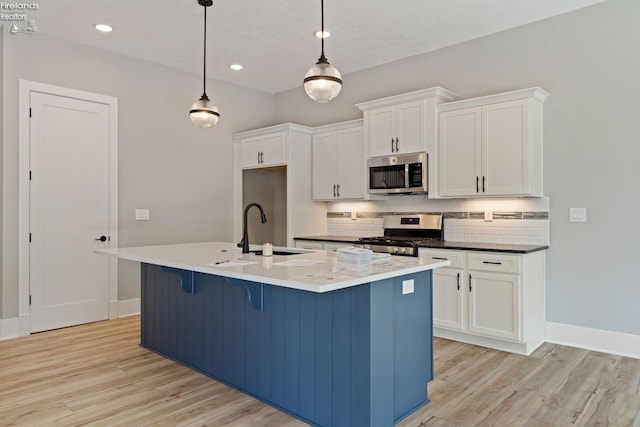 kitchen with a center island with sink, appliances with stainless steel finishes, hanging light fixtures, and light wood-type flooring