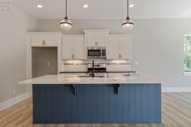 kitchen featuring appliances with stainless steel finishes, decorative light fixtures, and an island with sink