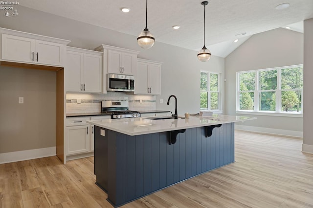 kitchen with a center island with sink, sink, pendant lighting, white cabinetry, and appliances with stainless steel finishes