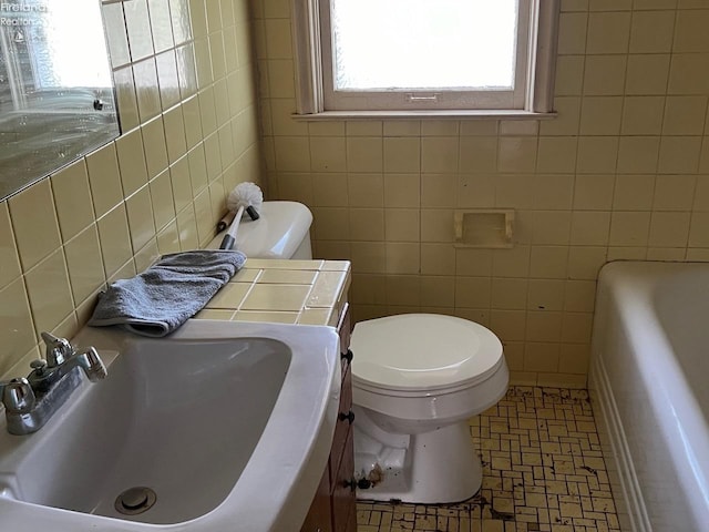 bathroom featuring toilet, sink, a bath, and tile walls