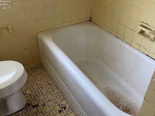 bathroom with tile walls, a tub to relax in, and toilet