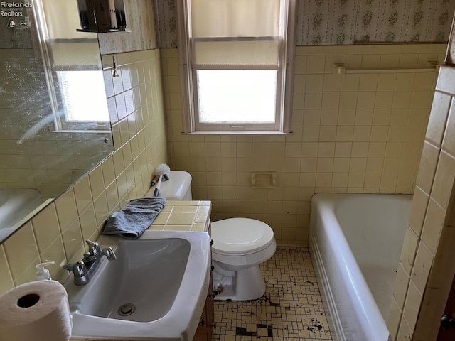 bathroom featuring tile walls, sink, a tub, and toilet