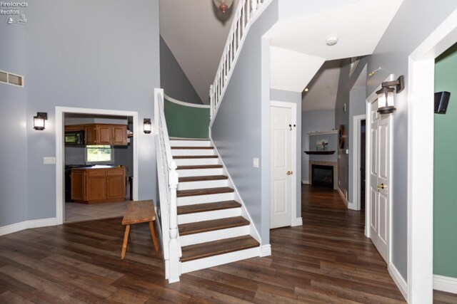 staircase featuring high vaulted ceiling and dark hardwood / wood-style flooring