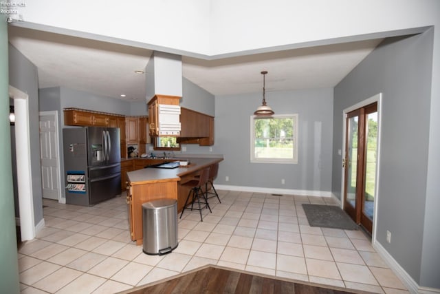 kitchen with pendant lighting, stainless steel refrigerator with ice dispenser, a kitchen bar, light tile patterned flooring, and kitchen peninsula