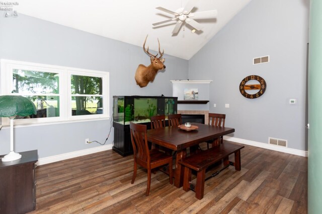 dining room featuring hardwood / wood-style flooring, a tile fireplace, high vaulted ceiling, and ceiling fan