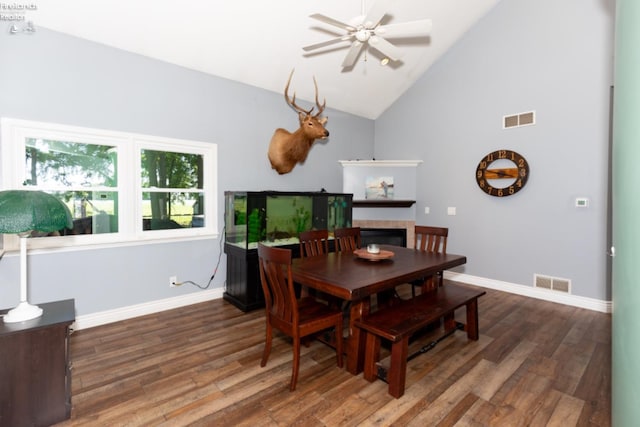 dining space with dark hardwood / wood-style floors, a tiled fireplace, and high vaulted ceiling