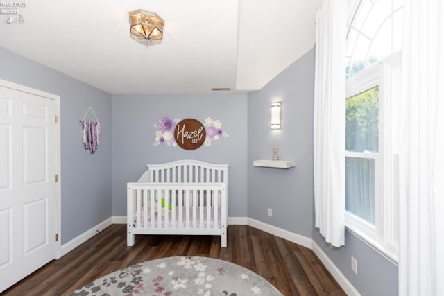 bedroom featuring a nursery area and dark hardwood / wood-style flooring