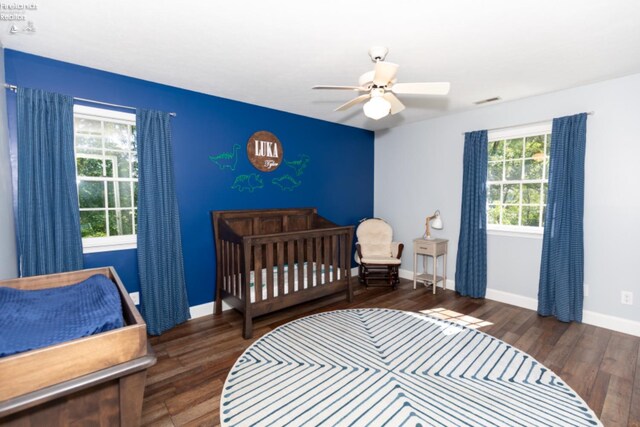 bedroom featuring dark hardwood / wood-style floors, a crib, and ceiling fan