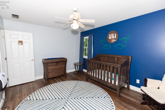 bedroom featuring wood-type flooring, a nursery area, and ceiling fan