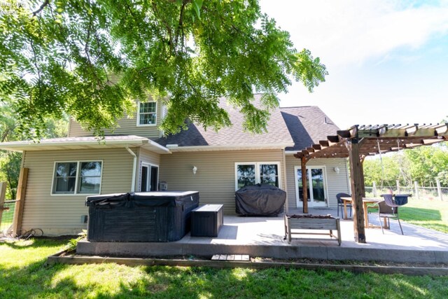 rear view of house with a hot tub, a yard, and a pergola