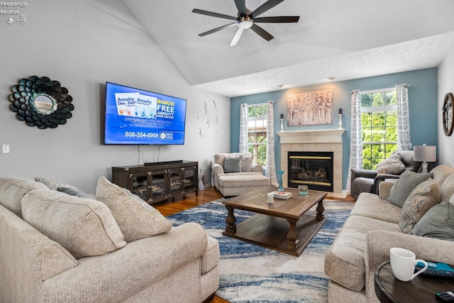 living room with wood-type flooring, ceiling fan, vaulted ceiling, a textured ceiling, and a tiled fireplace