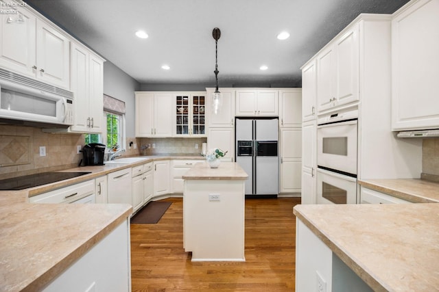 kitchen with white appliances, white cabinets, hanging light fixtures, hardwood / wood-style floors, and decorative backsplash