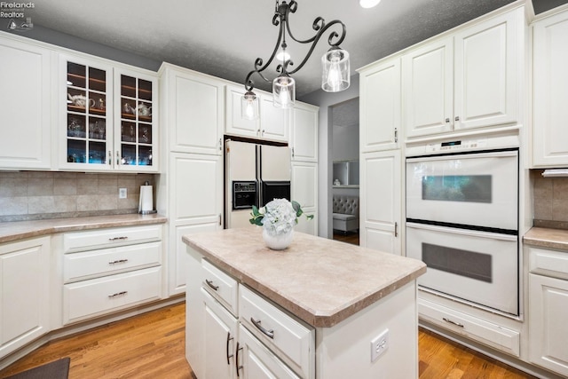 kitchen with decorative light fixtures, tasteful backsplash, light hardwood / wood-style flooring, and white appliances