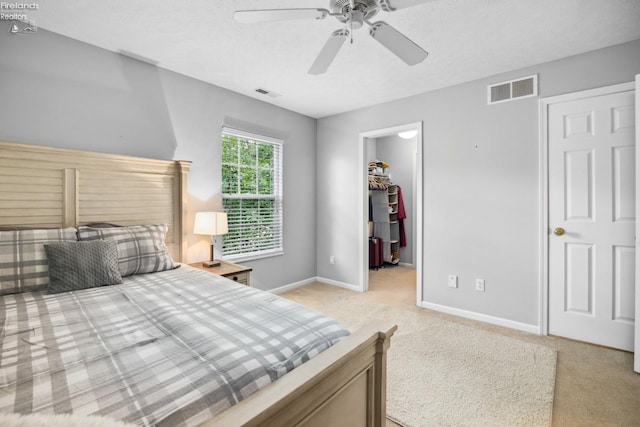 bedroom with light carpet, a closet, ceiling fan, and a walk in closet