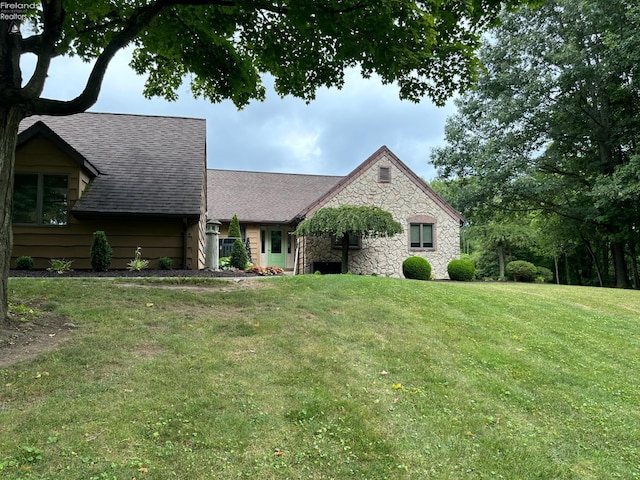 view of front of house featuring a front yard, stone siding, and roof with shingles