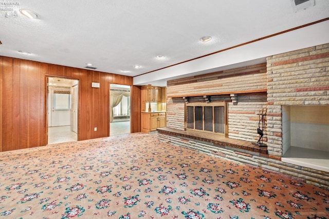 unfurnished living room featuring a textured ceiling, carpet floors, a brick fireplace, and wooden walls