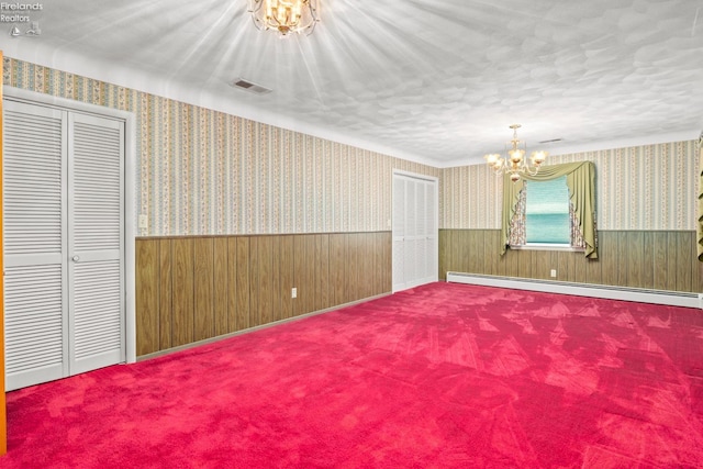 carpeted empty room featuring baseboard heating and a chandelier