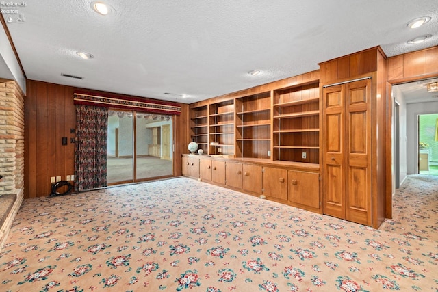 unfurnished living room featuring wood walls, light carpet, a textured ceiling, and brick wall