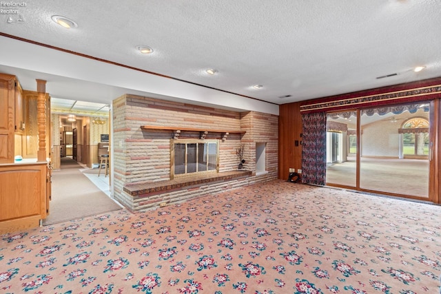 unfurnished living room featuring a fireplace, light carpet, wooden walls, and a textured ceiling