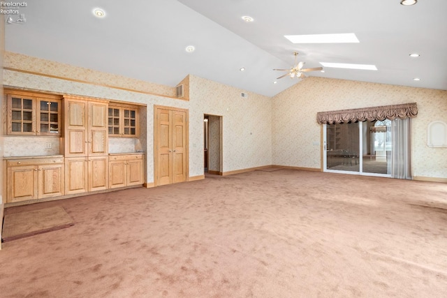 unfurnished living room featuring light carpet, lofted ceiling with skylight, and ceiling fan