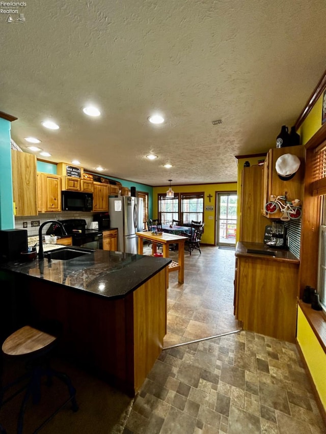 kitchen with recessed lighting, a peninsula, a sink, black appliances, and brown cabinetry