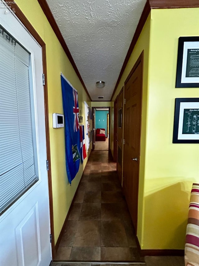 hallway featuring crown molding, baseboards, and a textured ceiling