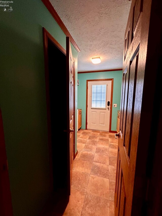 hallway with a textured ceiling, crown molding, and light tile patterned floors