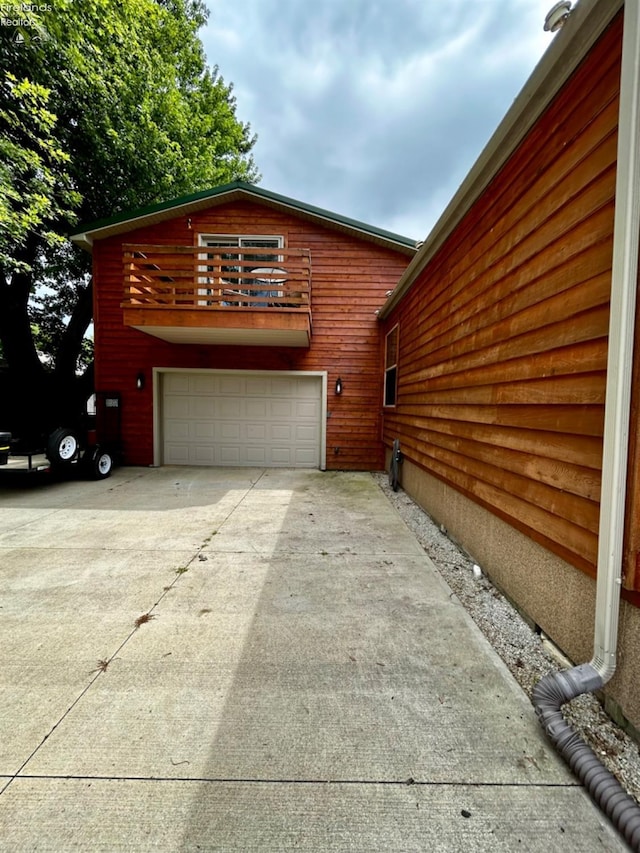 view of side of home with driveway, a balcony, and an attached garage