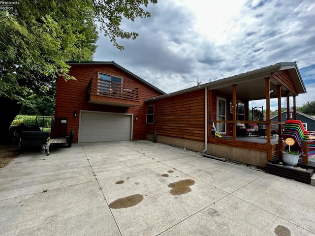 view of side of home featuring driveway, covered porch, an attached garage, and a balcony