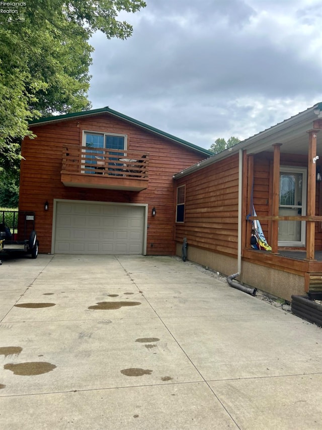 view of side of home with driveway, a balcony, and an attached garage