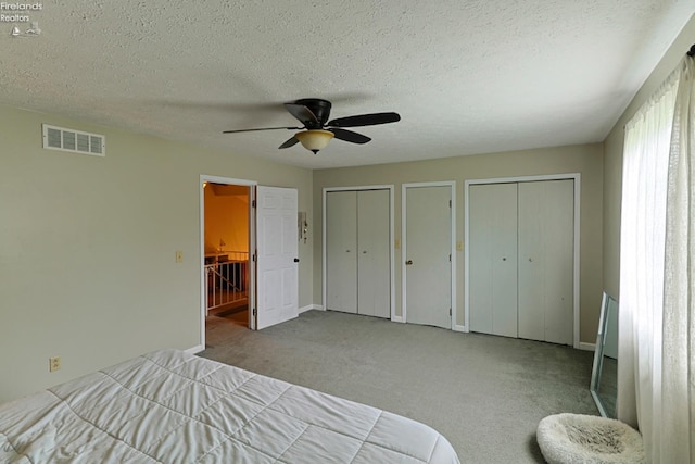 carpeted bedroom with multiple closets, a textured ceiling, and ceiling fan