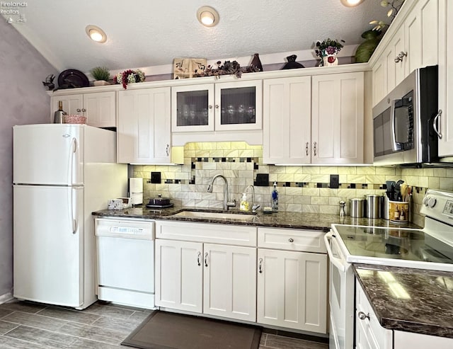 kitchen with white cabinetry, dark stone counters, white appliances, tasteful backsplash, and sink