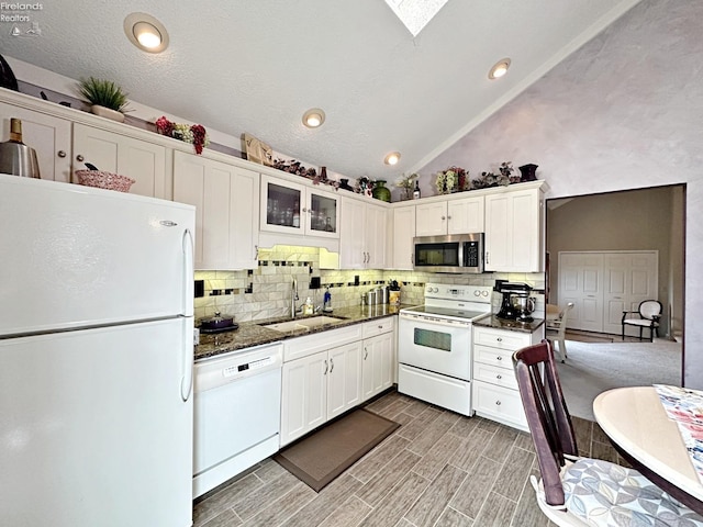 kitchen featuring white appliances, high vaulted ceiling, backsplash, dark stone counters, and sink